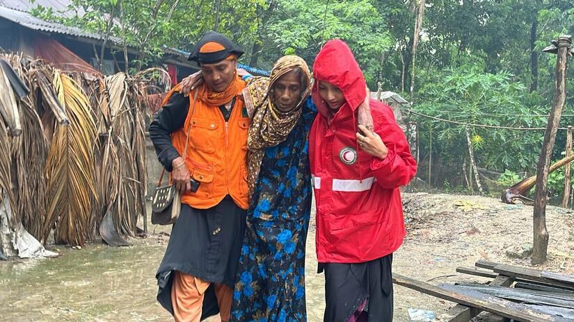 A Bangladesh Red Crescent volunteer helps a lady away from her flooded home following Cyclone Remal. The response was part funded through an IFRC-DREF allocation
Photo: BRCS